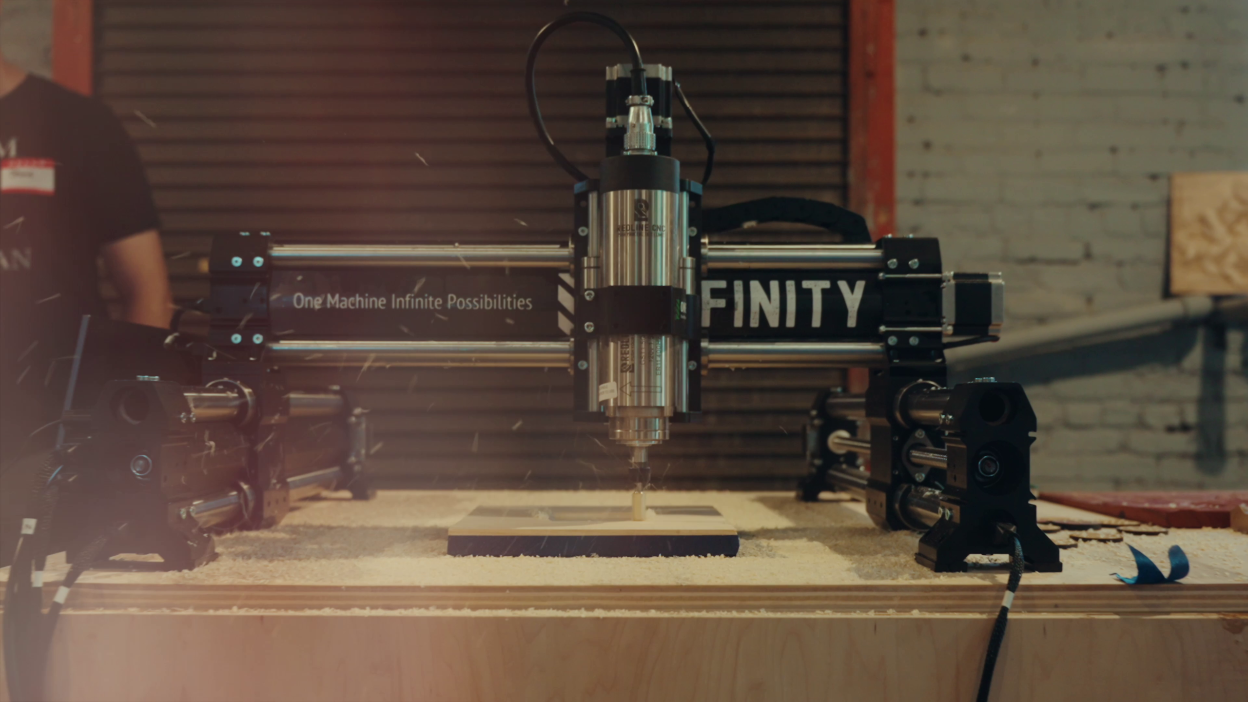 A Onefinity CNC machine carving a piece of wood, sawdust flying, with 'One Machine Infinite Possibilities' printed on the gantry