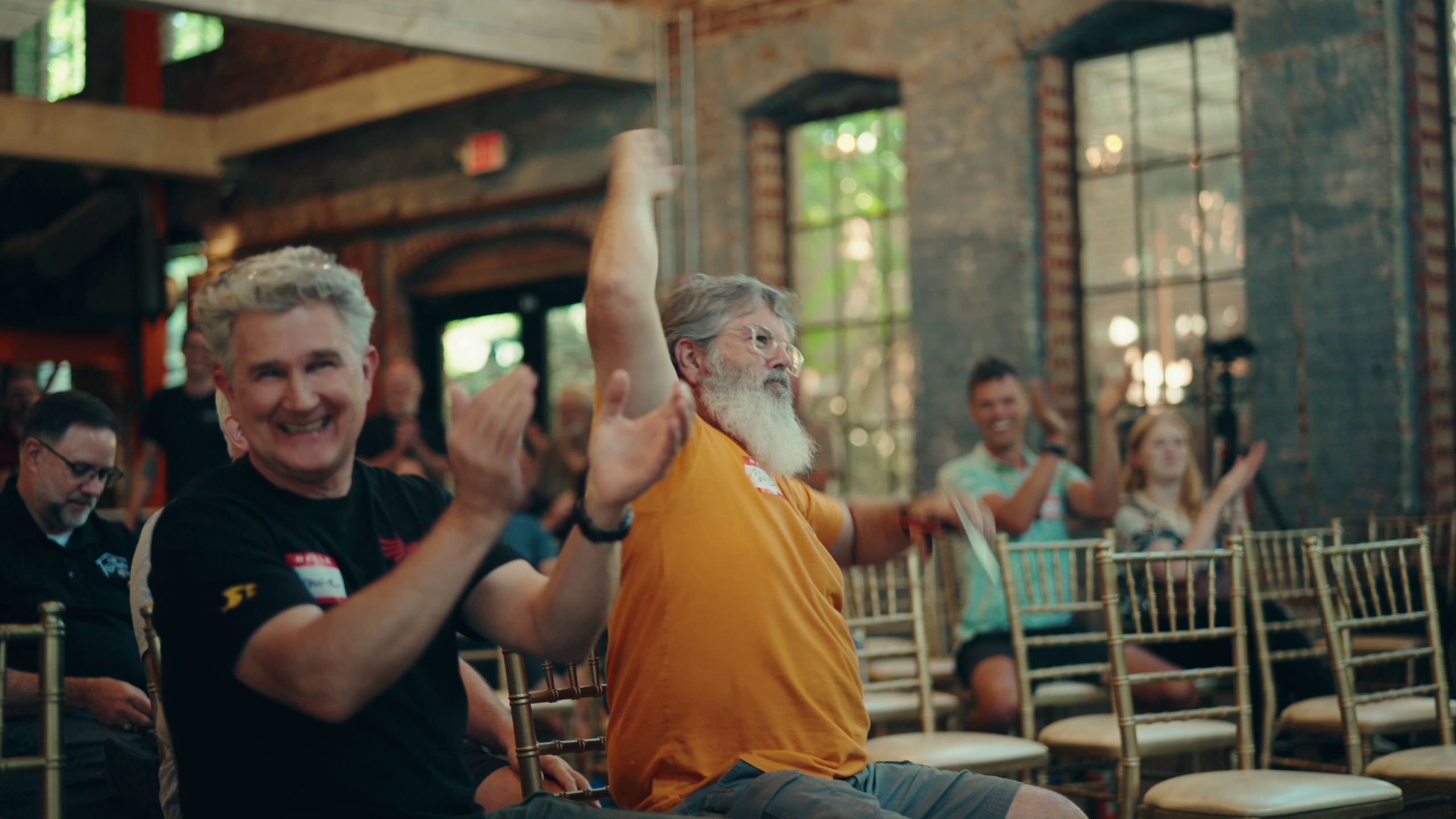 An attendee celebrates with arms raised, cheering the moment he won a CNC machine, as others around him applaud