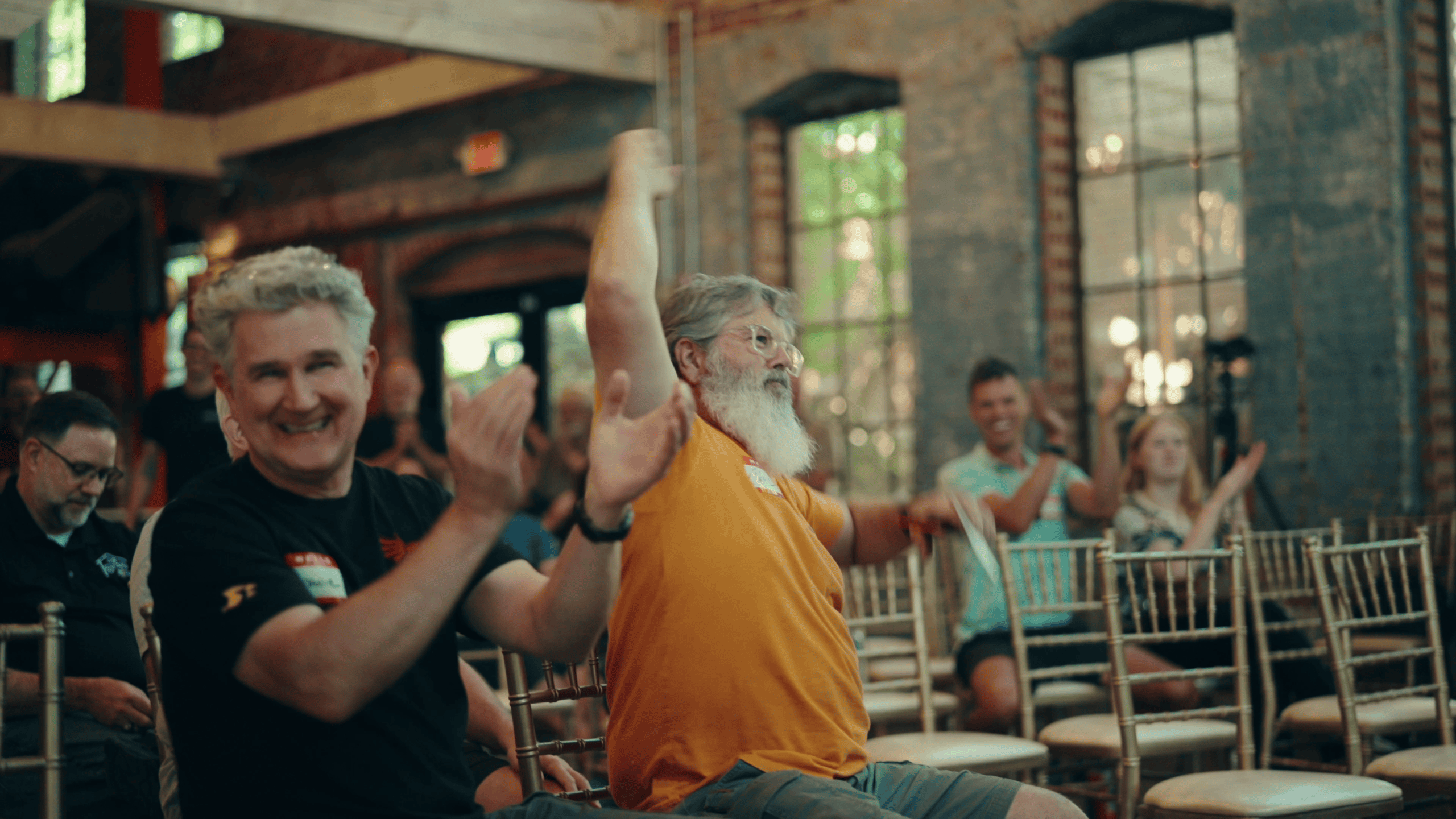 An attendee celebrates with arms raised, cheering the moment he won a CNC machine, as others around him applaud